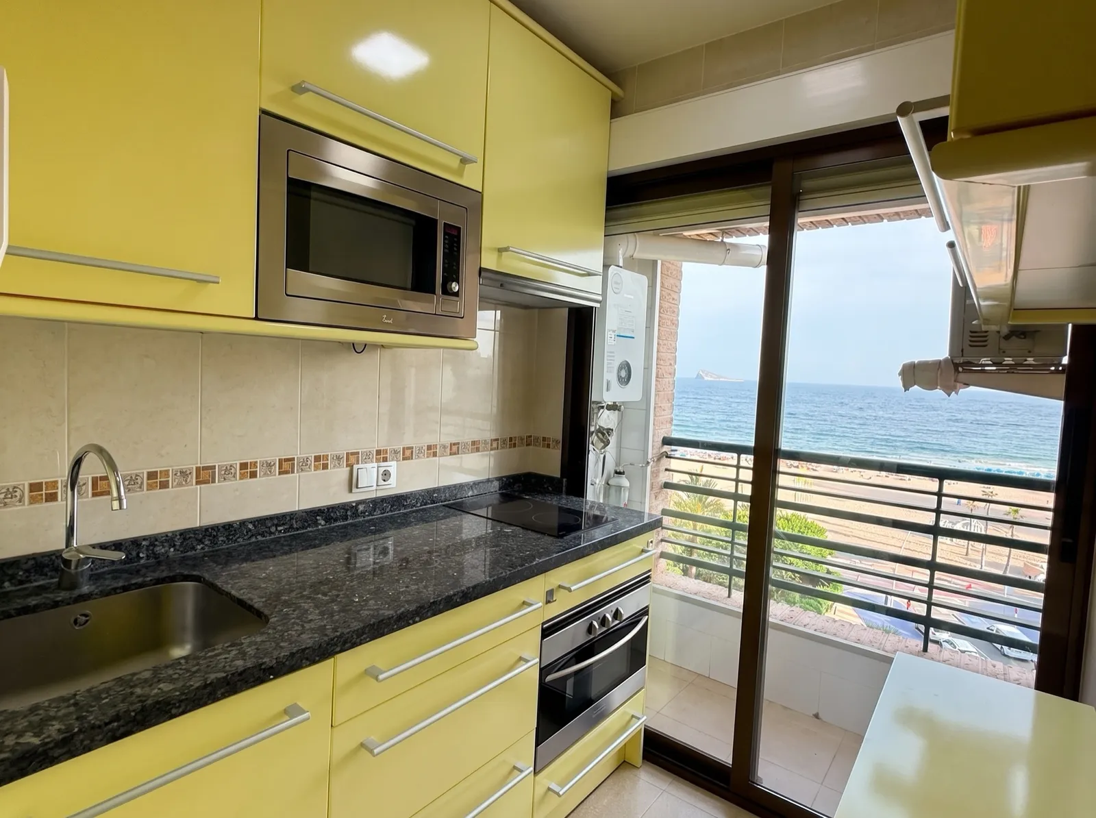 Cocina equipada con encimera de granito y salida a la terraza con vistas al mar